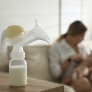 Mother feeding her little baby at home, focus on breast pump with milk. Healthy growth
